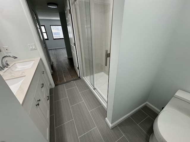 bathroom with a shower stall, baseboards, toilet, double vanity, and a sink