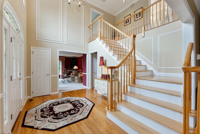 foyer with a notable chandelier, wood-type flooring, a high ceiling, and ornamental molding