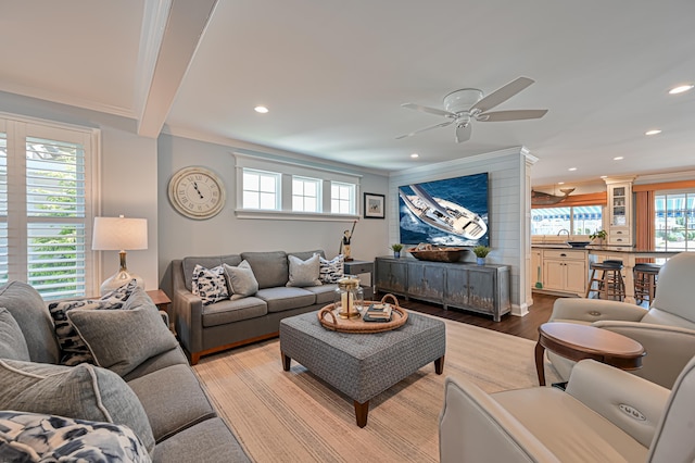 living room with ceiling fan, sink, light hardwood / wood-style flooring, beamed ceiling, and crown molding