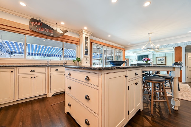 kitchen with a center island, dark wood-type flooring, a kitchen breakfast bar, decorative light fixtures, and ornamental molding