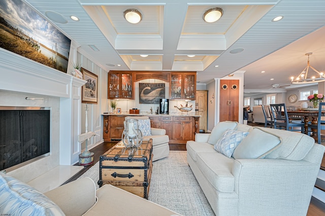 living room with beam ceiling, coffered ceiling, crown molding, a chandelier, and light wood-type flooring