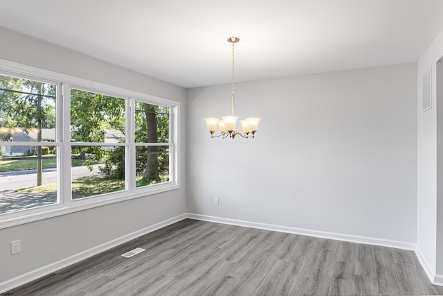 empty room featuring wood-type flooring and a notable chandelier