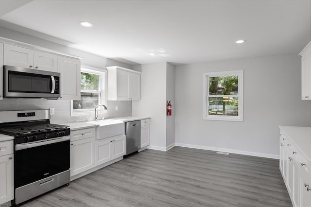 kitchen featuring backsplash, a wealth of natural light, appliances with stainless steel finishes, light hardwood / wood-style floors, and white cabinetry