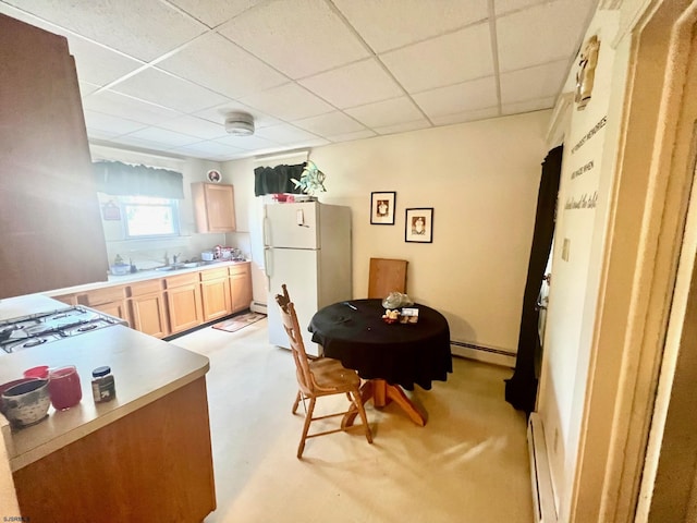 kitchen featuring a paneled ceiling, white refrigerator, light brown cabinetry, and a baseboard heating unit