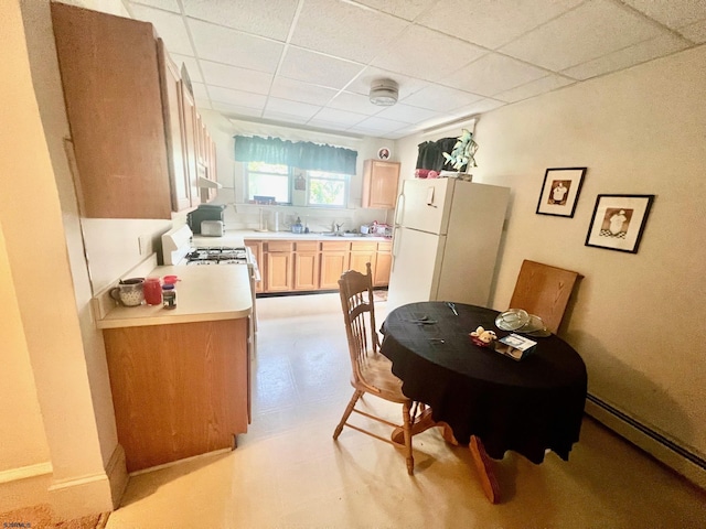 kitchen featuring light brown cabinets, sink, a baseboard heating unit, white refrigerator, and a paneled ceiling