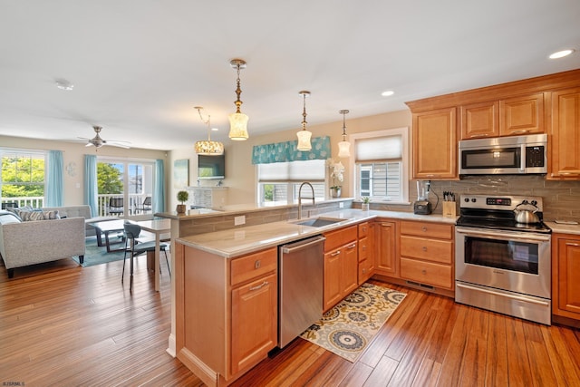 kitchen with sink, stainless steel appliances, decorative light fixtures, kitchen peninsula, and light wood-type flooring