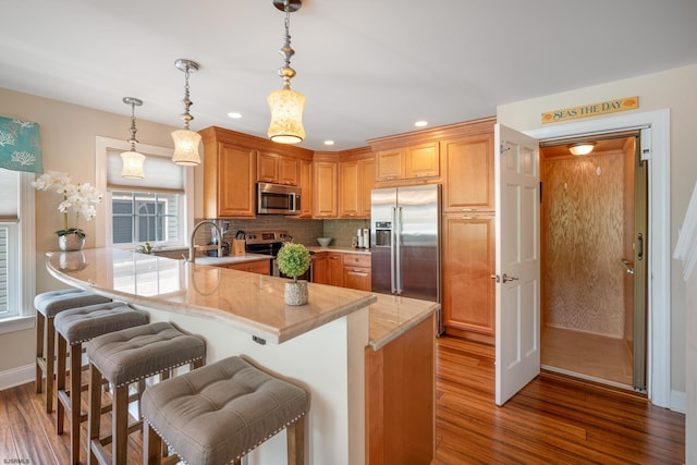 kitchen featuring appliances with stainless steel finishes, hanging light fixtures, a kitchen bar, decorative backsplash, and kitchen peninsula