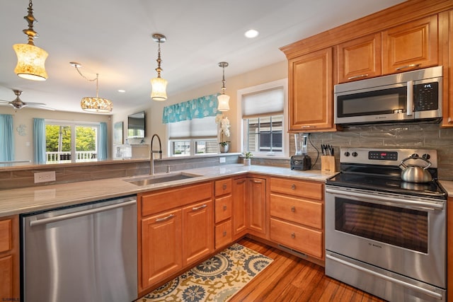 kitchen with sink, light hardwood / wood-style flooring, appliances with stainless steel finishes, decorative backsplash, and decorative light fixtures