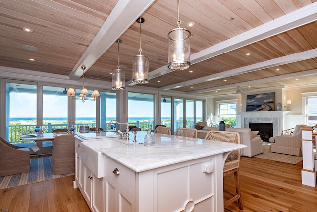 kitchen featuring an island with sink, decorative light fixtures, a premium fireplace, white cabinets, and light stone counters