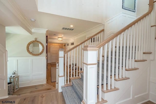 stairway with wood-type flooring and crown molding