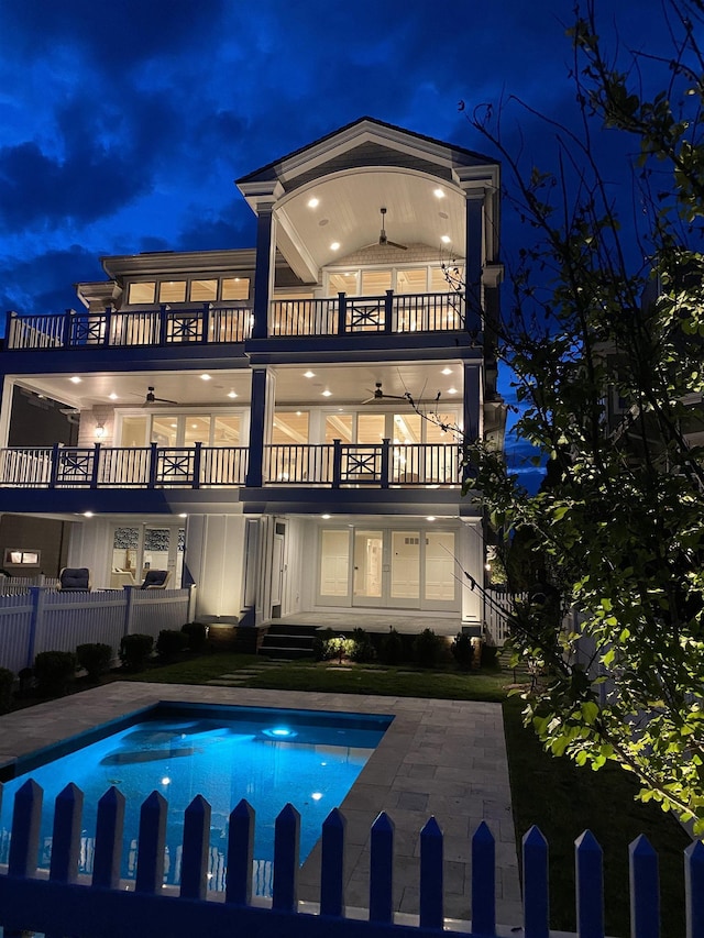 back house at twilight with ceiling fan, a patio, a balcony, and a fenced in pool