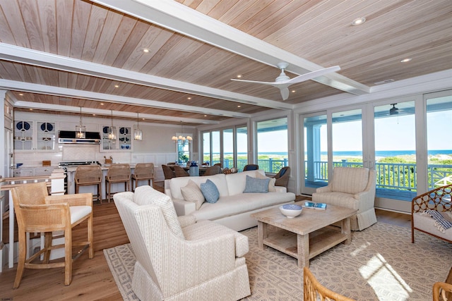 living room featuring beam ceiling, ceiling fan with notable chandelier, and light hardwood / wood-style flooring