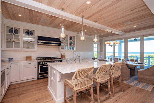 kitchen with extractor fan, white cabinetry, beamed ceiling, an island with sink, and double oven range