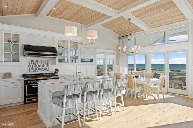 kitchen with double oven range, exhaust hood, white cabinetry, wooden ceiling, and a water view