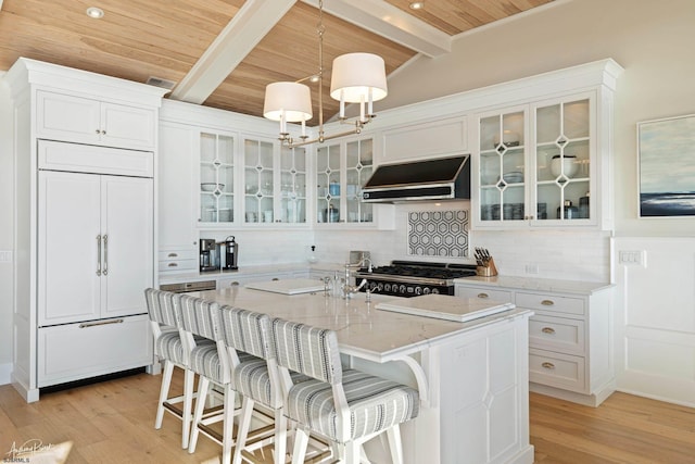 kitchen featuring paneled built in fridge, backsplash, a kitchen island with sink, stove, and range hood