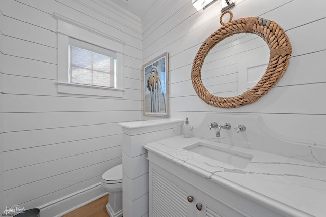 bathroom featuring toilet, vanity, and wood walls