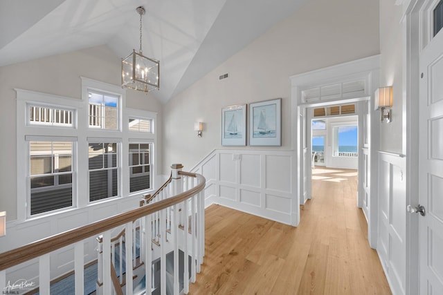 hallway featuring high vaulted ceiling, light wood-type flooring, and an inviting chandelier