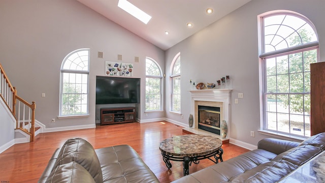 living room with a skylight, light hardwood / wood-style flooring, high vaulted ceiling, and a premium fireplace