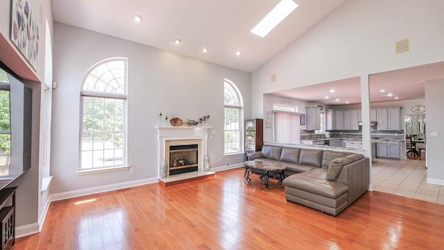 living room with a skylight, high vaulted ceiling, and light hardwood / wood-style flooring