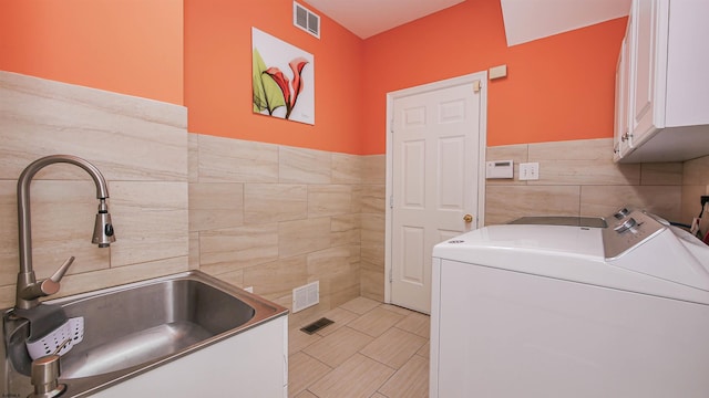 laundry area featuring cabinets, sink, tile walls, and independent washer and dryer