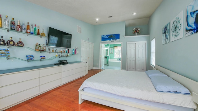 bedroom with hardwood / wood-style floors, a towering ceiling, bar, and ensuite bath