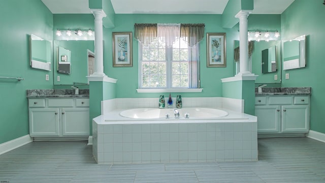 bathroom with vanity, decorative columns, and tiled tub