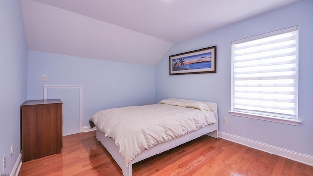 bedroom with vaulted ceiling, hardwood / wood-style floors, and multiple windows