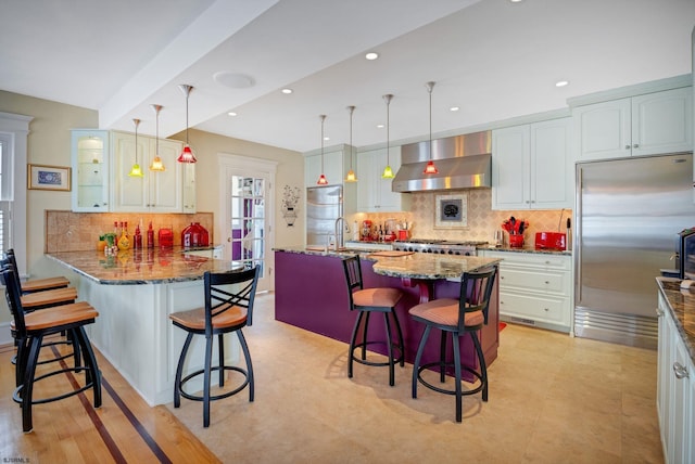 kitchen featuring a breakfast bar, pendant lighting, appliances with stainless steel finishes, dark stone countertops, and ventilation hood