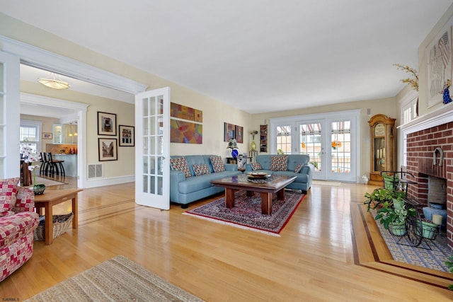 living room featuring wood finished floors, visible vents, baseboards, french doors, and a brick fireplace