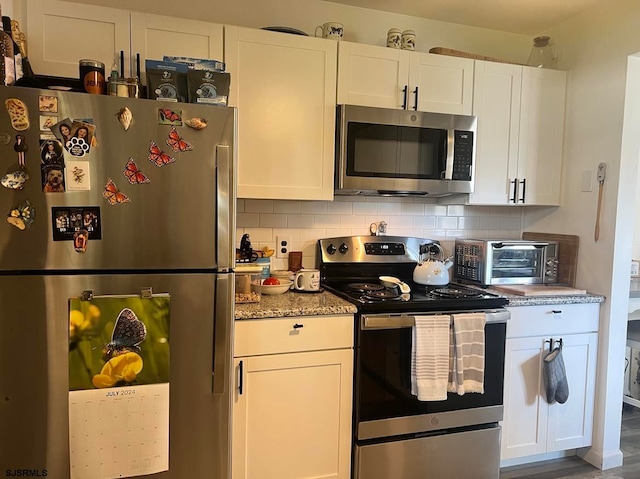 kitchen with stainless steel appliances, hardwood / wood-style floors, white cabinets, backsplash, and light stone countertops