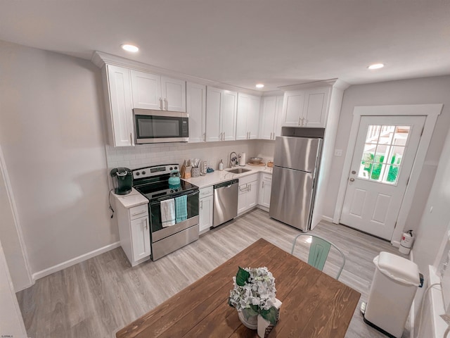 kitchen featuring sink, stainless steel appliances, white cabinets, decorative backsplash, and light hardwood / wood-style flooring