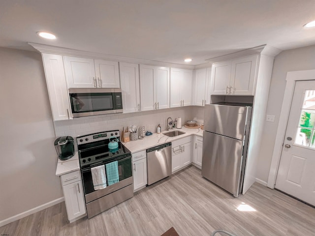 kitchen featuring appliances with stainless steel finishes, sink, backsplash, light hardwood / wood-style floors, and white cabinets