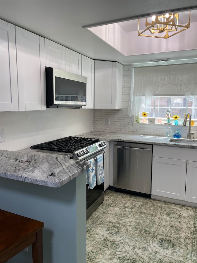 kitchen with an inviting chandelier, white cabinets, stainless steel appliances, decorative backsplash, and sink