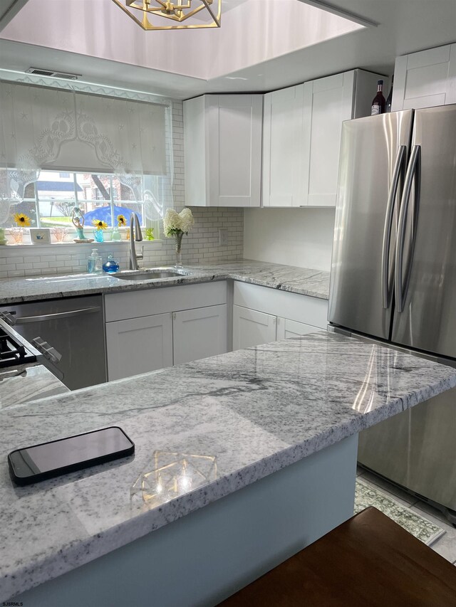 kitchen featuring white cabinets, decorative backsplash, light stone counters, and stainless steel appliances