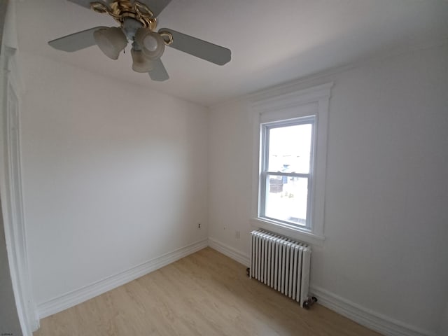 spare room with light wood-type flooring, ceiling fan, and radiator