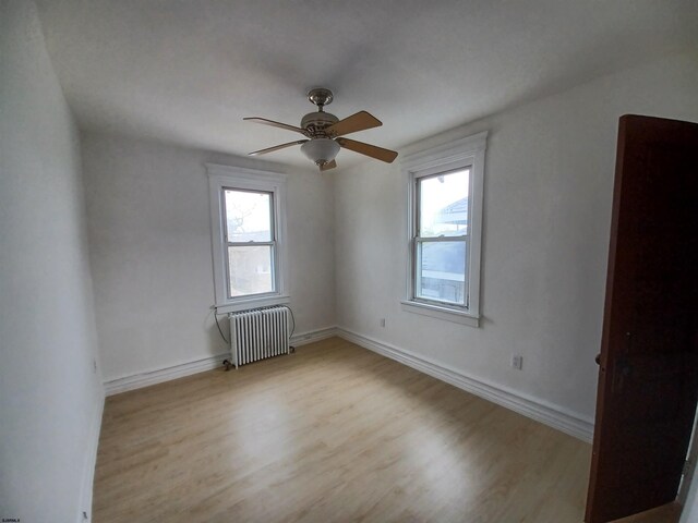 spare room with radiator heating unit, ceiling fan, and light wood-type flooring