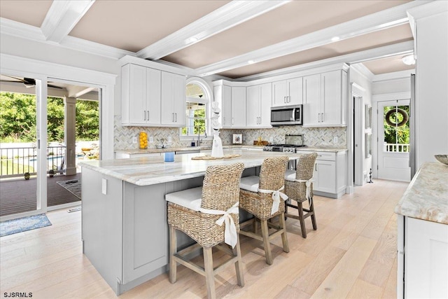 kitchen featuring light wood-type flooring, a kitchen breakfast bar, a kitchen island, white cabinetry, and beamed ceiling