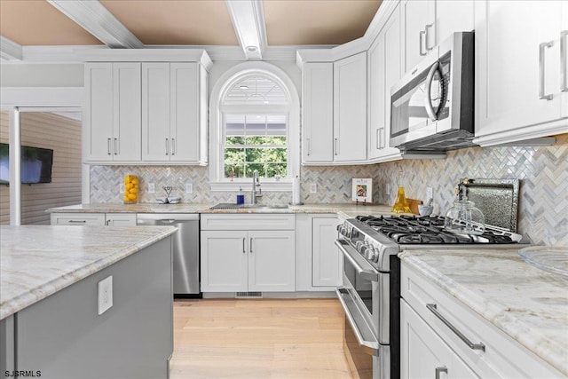 kitchen with stainless steel appliances, beam ceiling, white cabinets, light hardwood / wood-style flooring, and sink