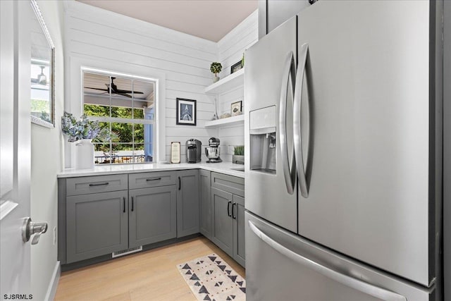 kitchen featuring stainless steel fridge with ice dispenser, light hardwood / wood-style flooring, gray cabinetry, and wooden walls