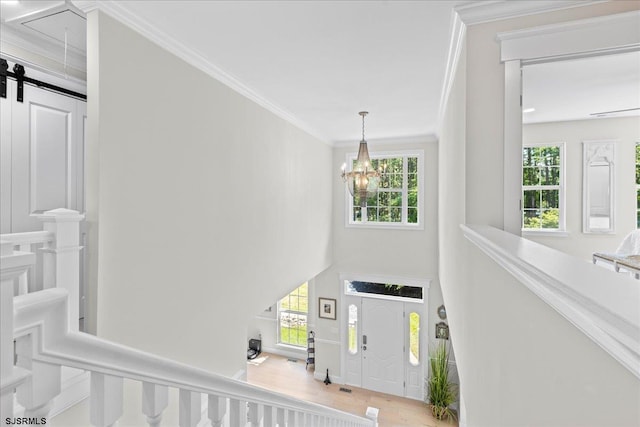 entrance foyer featuring light hardwood / wood-style flooring, a barn door, a chandelier, and crown molding