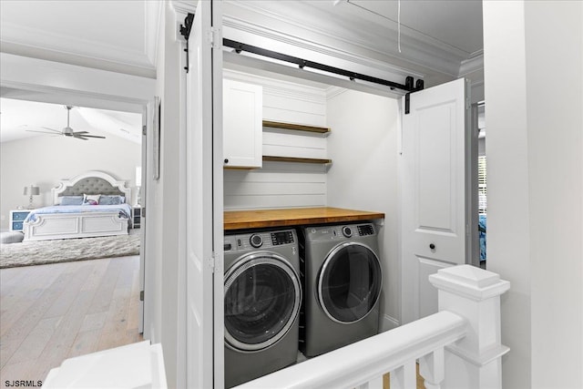 clothes washing area with ceiling fan, cabinets, wood-type flooring, a barn door, and washer and clothes dryer