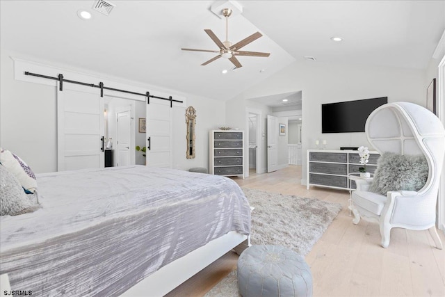 bedroom featuring lofted ceiling, light wood-type flooring, a barn door, and ceiling fan