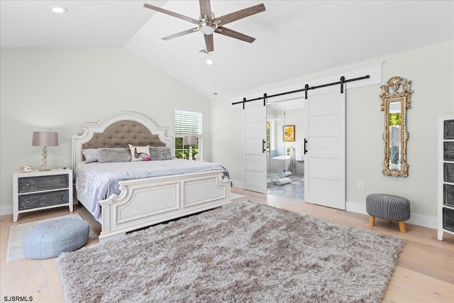 bedroom featuring light wood-type flooring, high vaulted ceiling, ensuite bath, ceiling fan, and a barn door