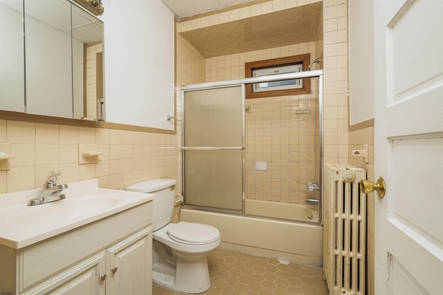 full bathroom with radiator, tile walls, bath / shower combo with glass door, vanity, and toilet