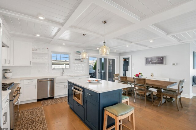 kitchen with tasteful backsplash, appliances with stainless steel finishes, coffered ceiling, wood-type flooring, and a kitchen island