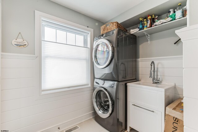 laundry room featuring cabinets, sink, and stacked washer and clothes dryer