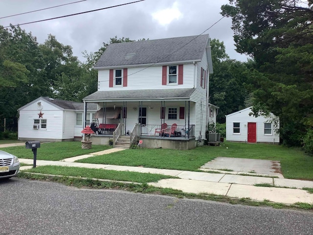 view of front facade with a porch, a front yard, and an outbuilding