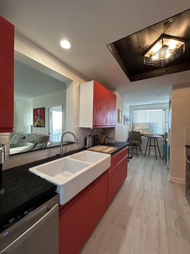 kitchen with dark countertops, decorative backsplash, a sink, light wood-type flooring, and dishwasher