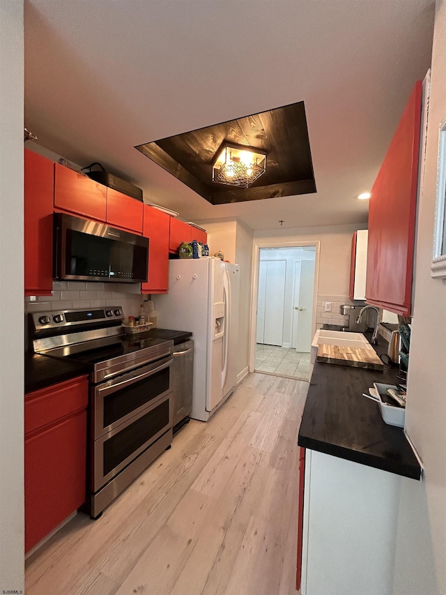 kitchen featuring stainless steel appliances, a tray ceiling, dark countertops, and tasteful backsplash