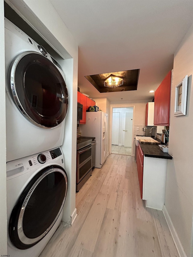 washroom featuring a sink, stacked washing maching and dryer, light wood-type flooring, laundry area, and baseboards